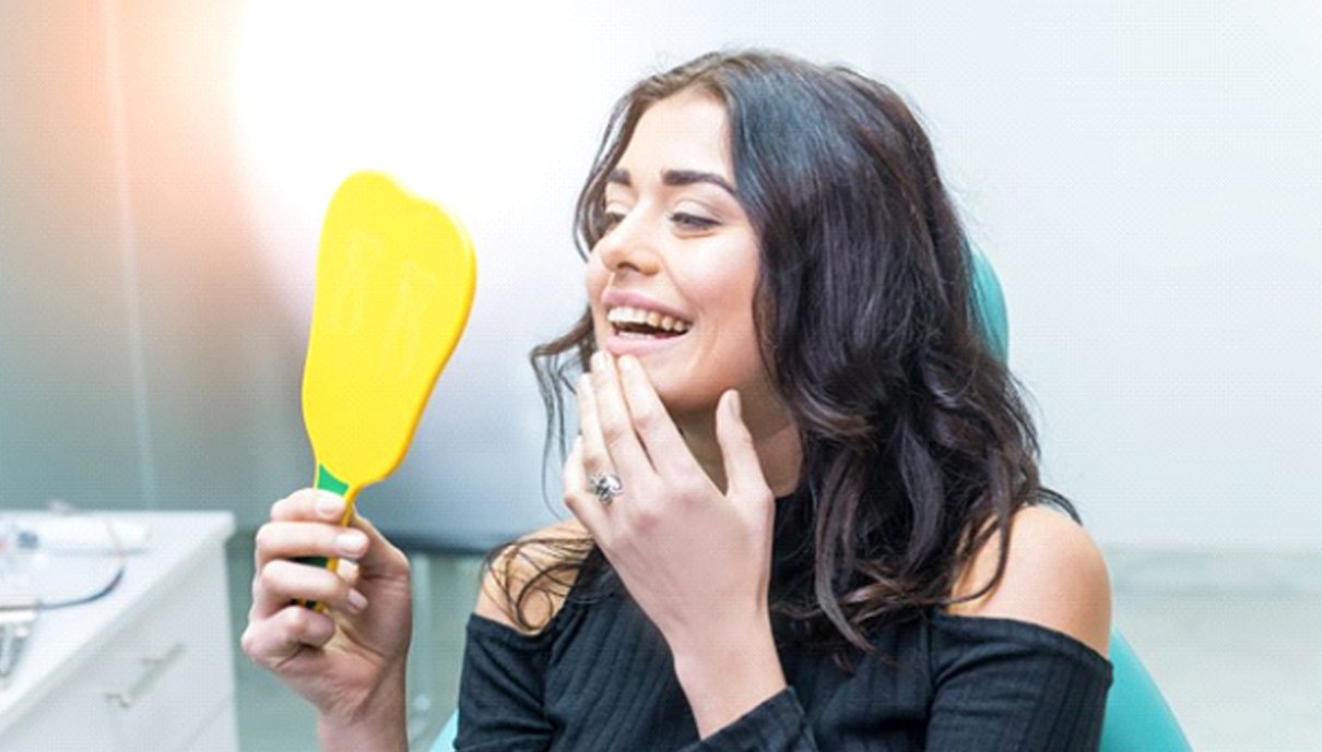 patient admiring her new smile in a mirror after getting dental crowns in Mission Viejo, CA