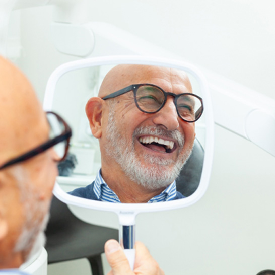 Man with black glasses smiling in reflection in mirror