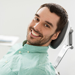Man in dentist’s chair smiling after overcoming dental emergency 