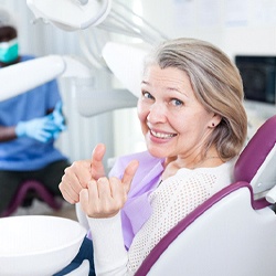 Older woman smiling in dental chair with two thumbs up