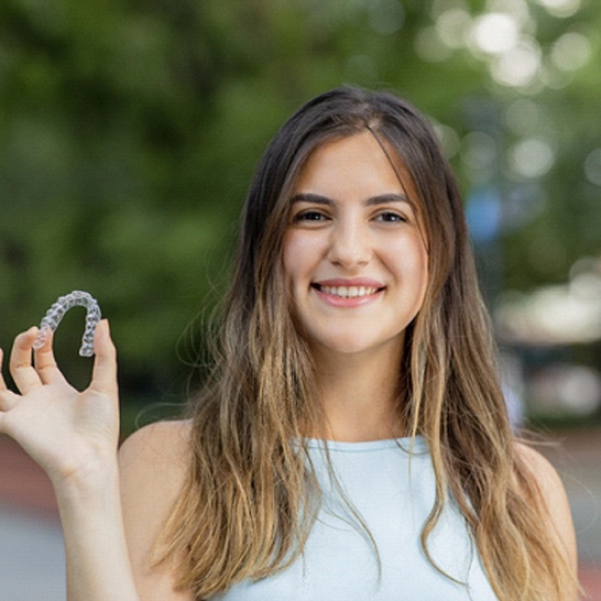 Smiling woman holding Invisalign in Mission Viejo outside