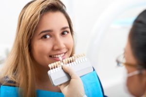 dentist holding a row of veneers up to a young woman’s smile 