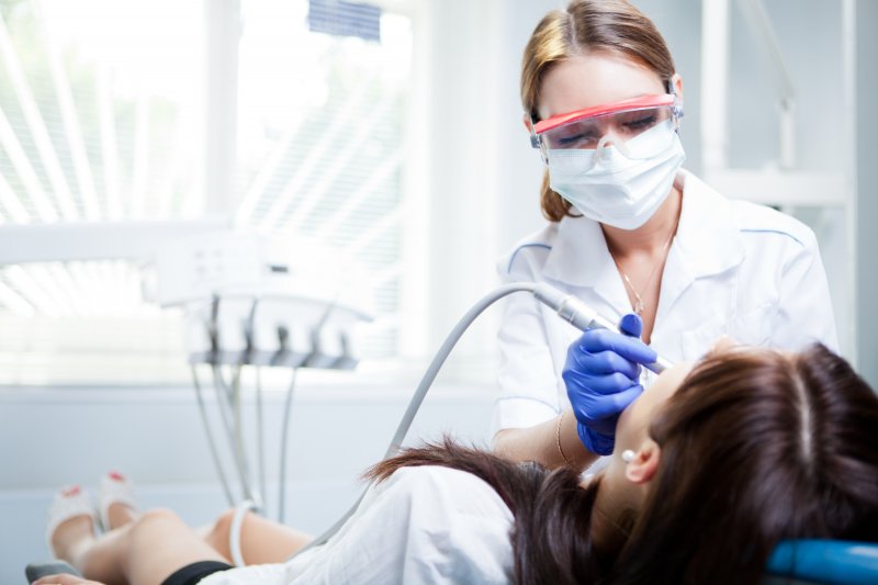 Dentist using cleaning tool on female patient laying in dental chair