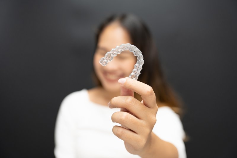A woman holding up her Invisalign aligner with a smile