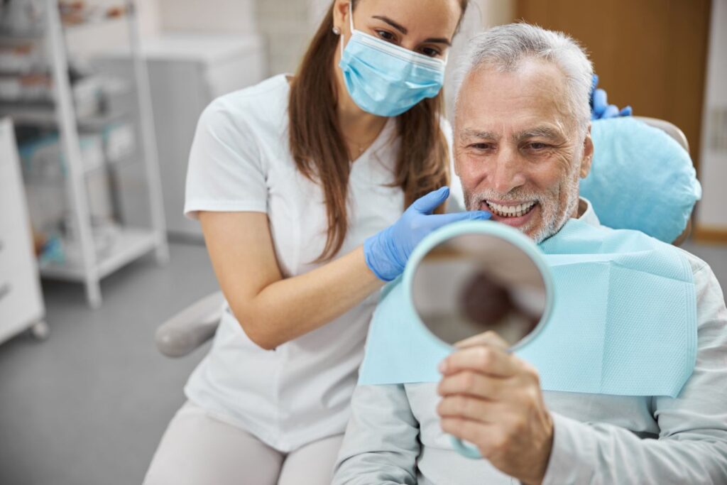 A man looking at his new dental implants in the mirror at the dentist's office.